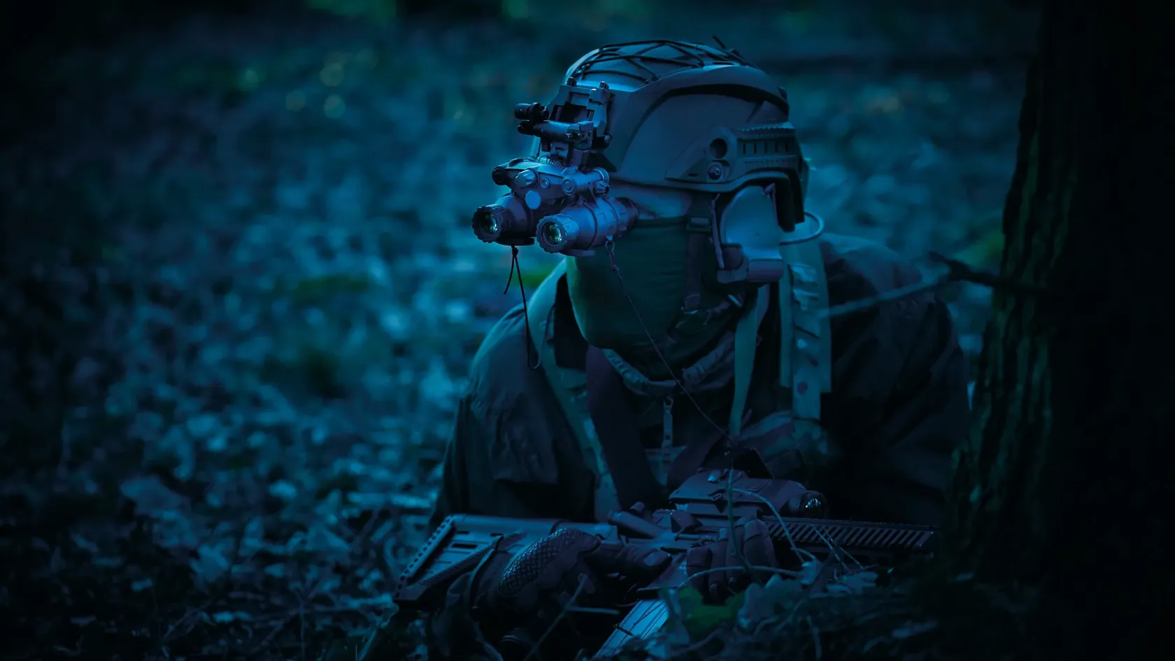 Operator in low light wearing a helmet-mounted night-vision device in a wooded environment.